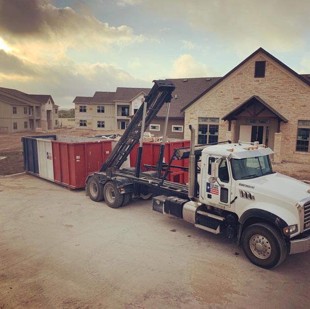 Truck dropping off a dumpster in front of a building project